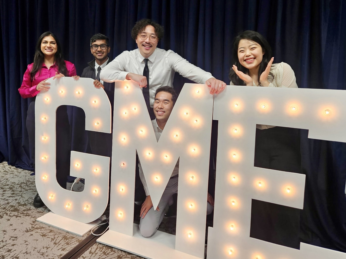 Photo showing of a group of man and woman, the new residents and fellows of Riverside Community Hospital, next to light up letters signs-that says "GME".