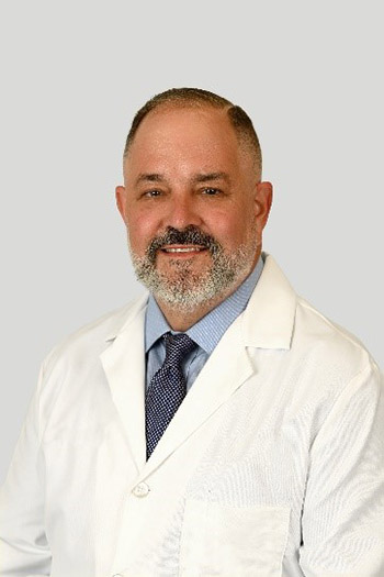 Dr. Mark Borowicz, wearing a dress shirt and tie under a white lab coat.