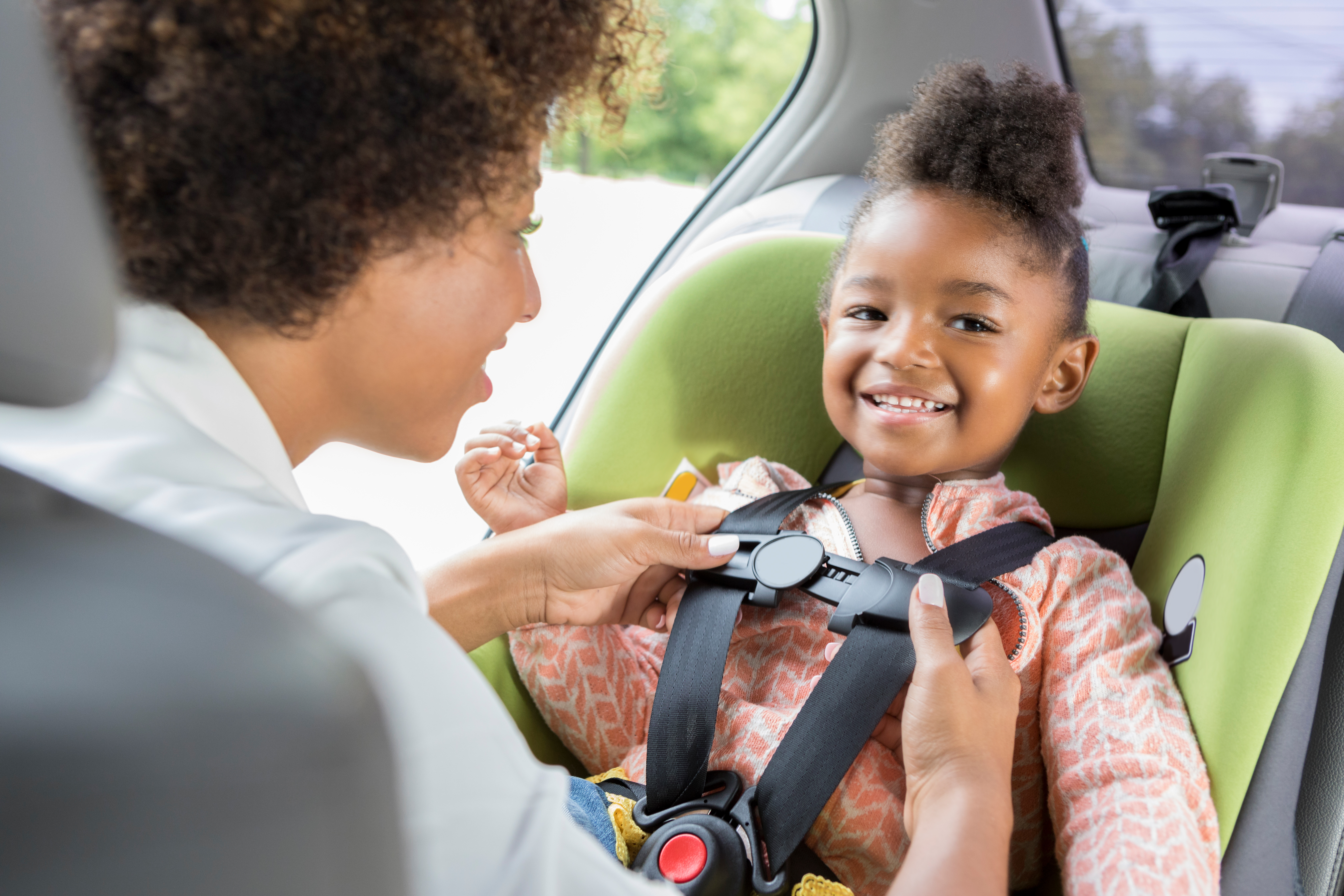 Young mom buckling female toddler into car seat.