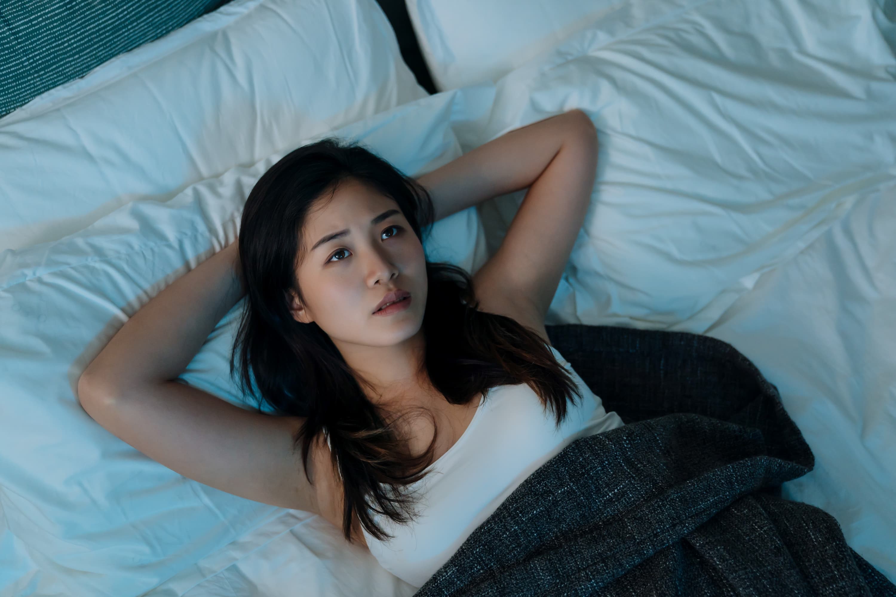A woman lying in bed looking up at the ceiling, unable to sleep at night.