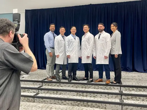 Group of female and male medical residents wearing medical jackets pose for photo.