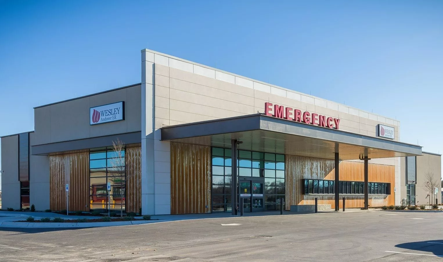 Exterior of Andover ER. A single floor tan and white building with wood paneling along the front and side, mirrored windows and a red sign that reads EMERGENCY above the front awning.