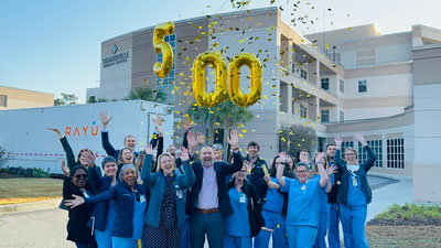 Employees celebrates with balloons and confetti in front of hospital.