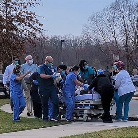 Donald Hurt is encircled by numerous Spotsylvania Regional Medical Center staff transporting him via hospital bed alongside an exterior sidewalk. 
