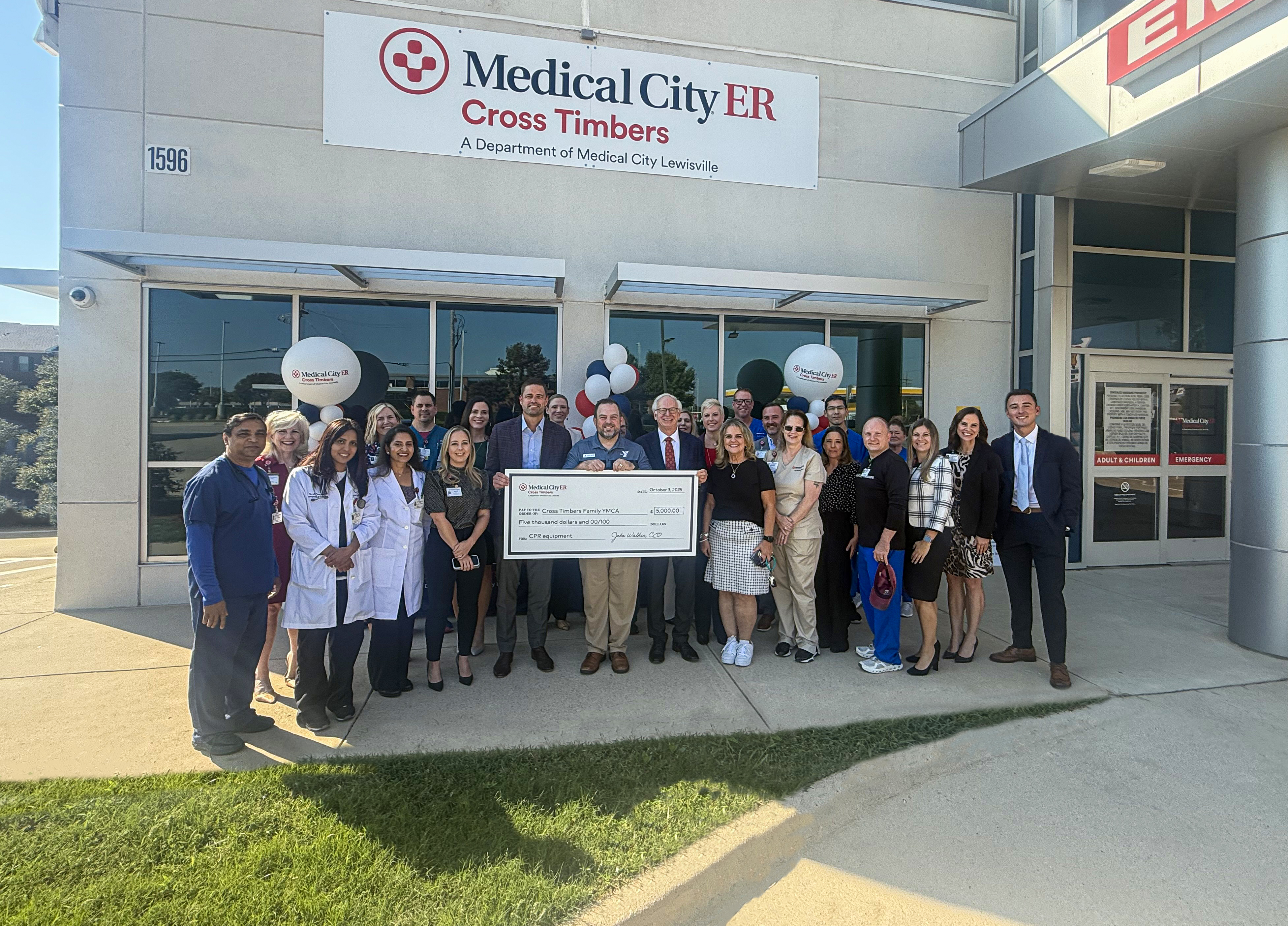 Medical City team members stand outside of Cross Timbers ER holding giant check representing $5,000 donation.