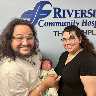 The Garcia family smiles while standing together, holding their newborn.