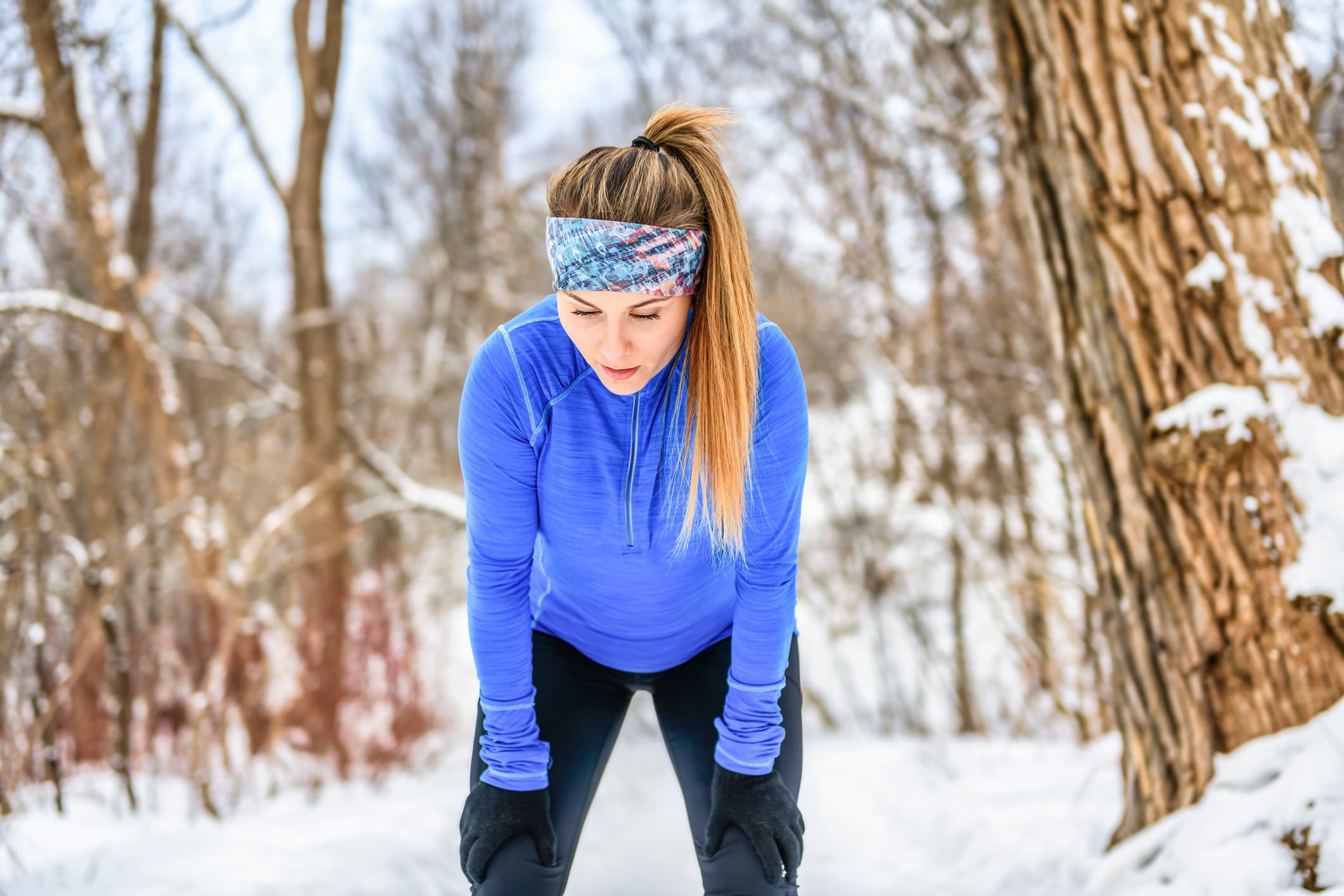 Young woman feeling pain in legs after jogging outside in winter park.