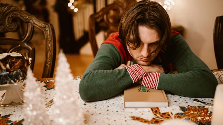 A person looking stressed out sitting at a table with a book and holiday decor