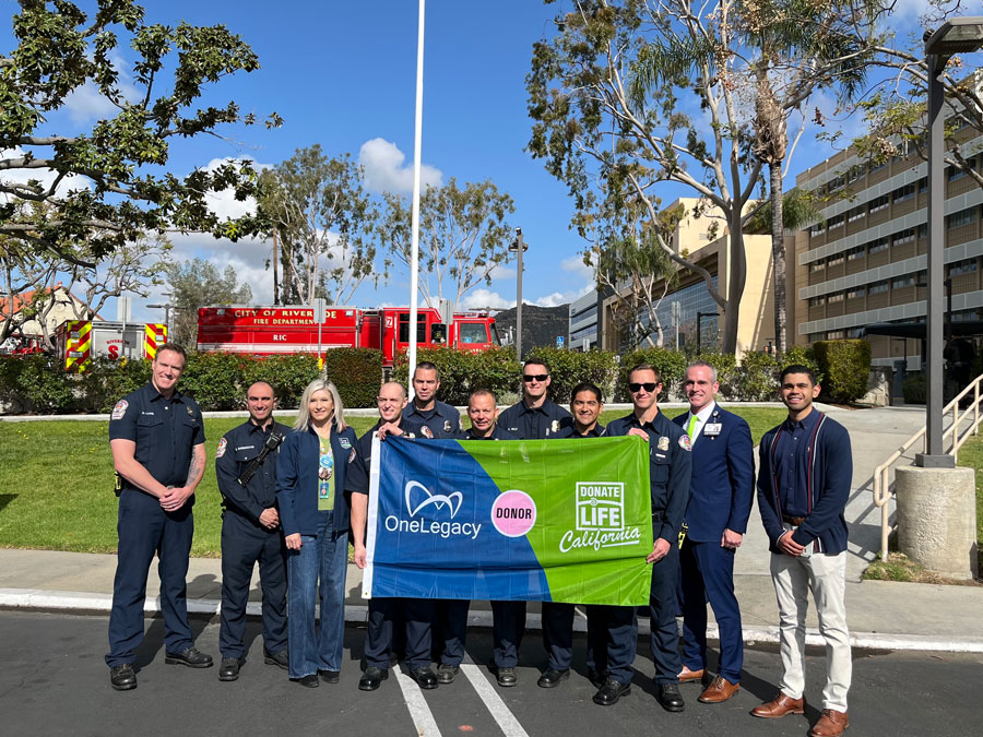 A group of medical professionals from Riverside Community Hospital smile while standing together, holding a flag with the Donate Life logo.