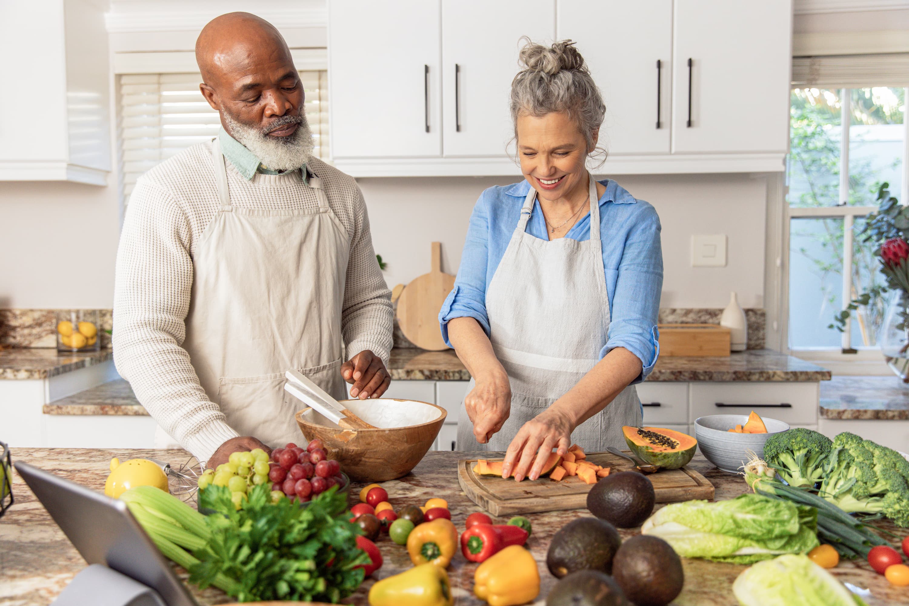 Two adults preparing a meal together in a kitchen, chopping vegetables and arranging fresh ingredients on a counter.