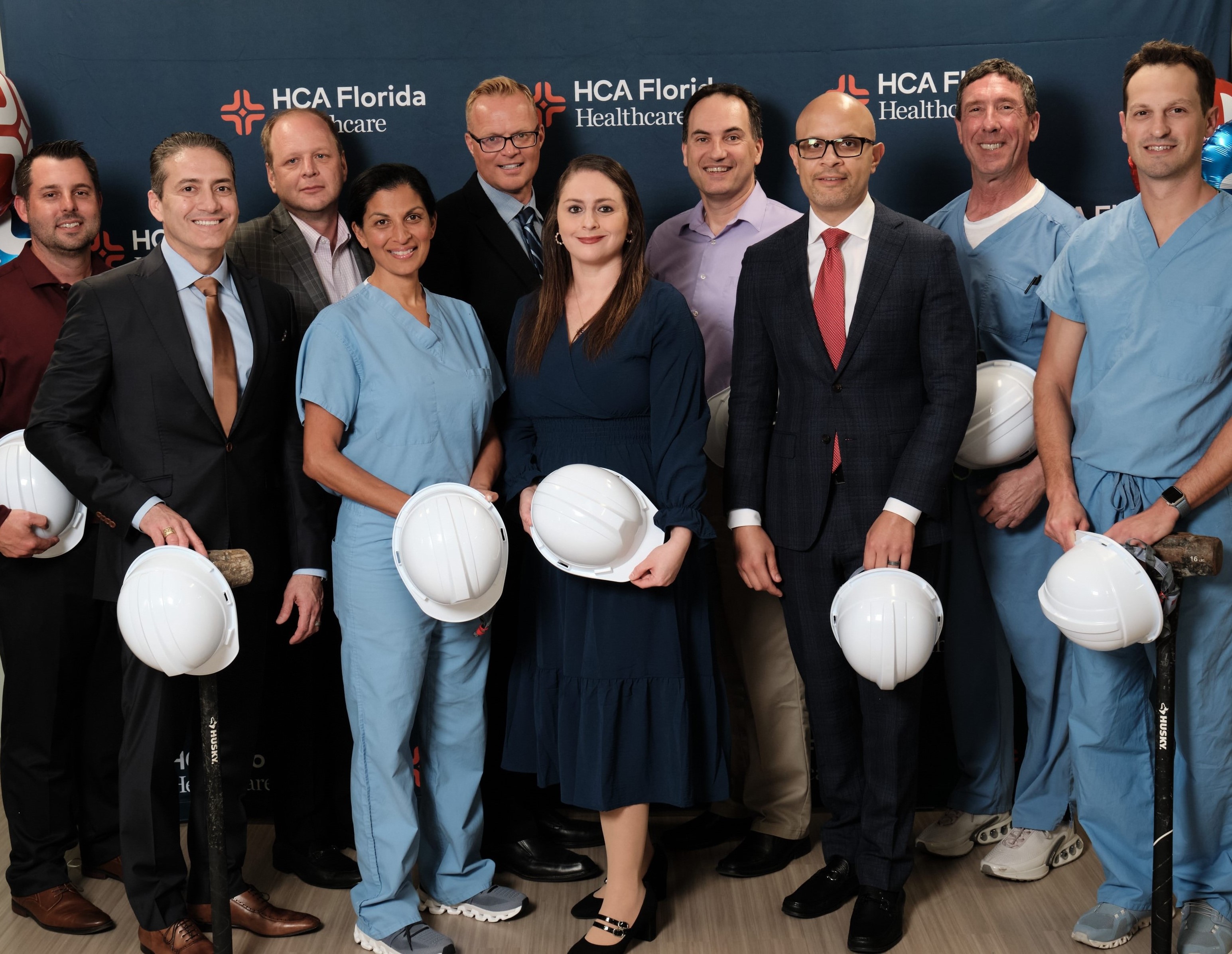 Hospital executives and medical staff pose with hardhats and sledgehammers in hand.