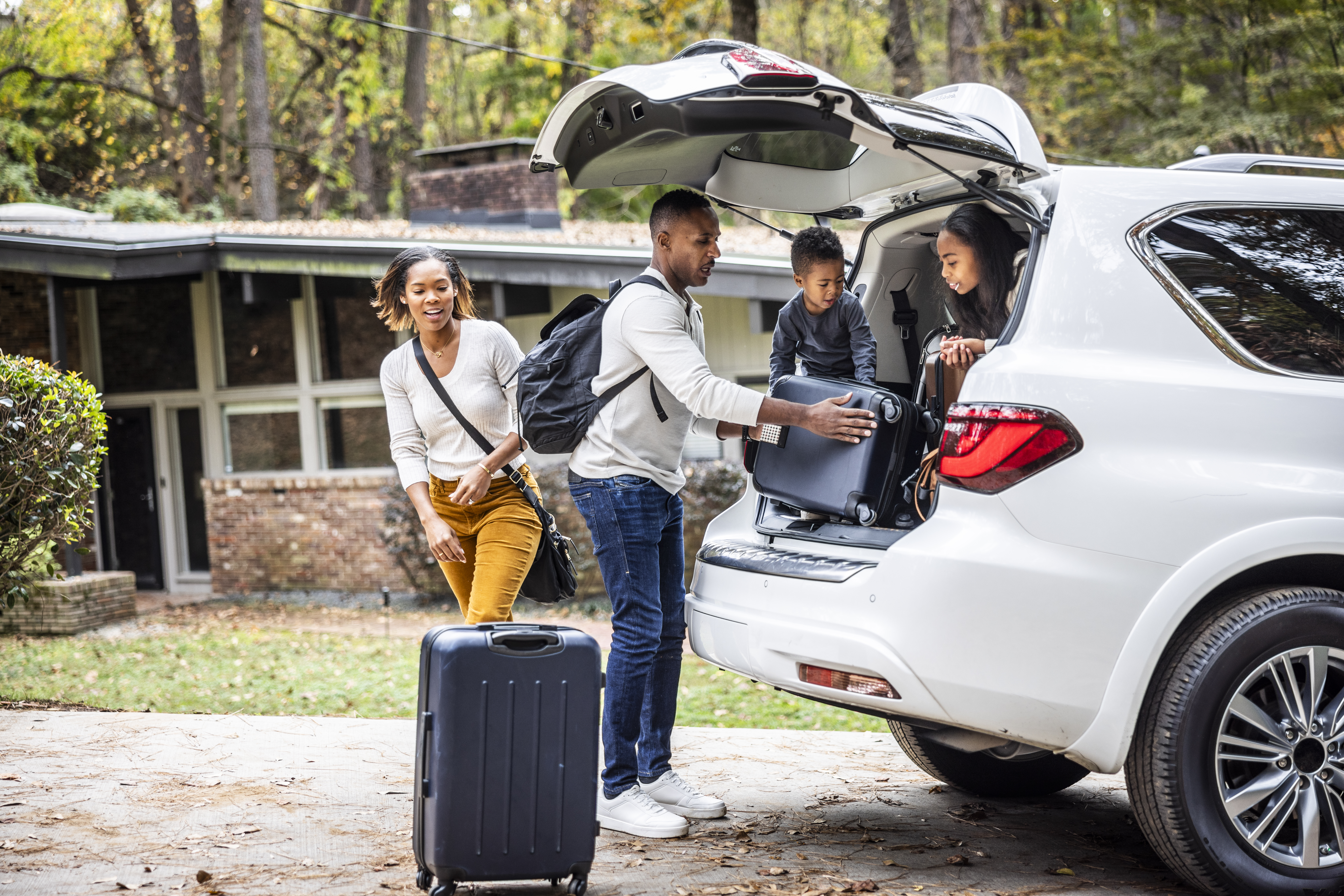 Children help parents load luggage into the back of an SUV.