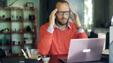 A man holds his temples with his eyes closed, trying to soothe a headache.