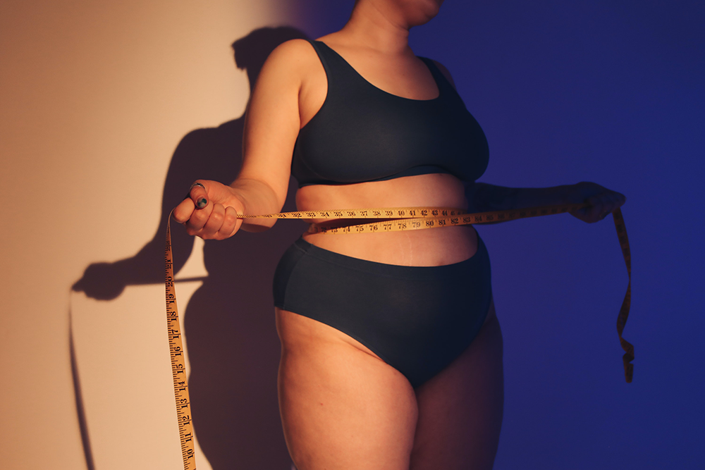 A woman wraps a tape measure around her waist.