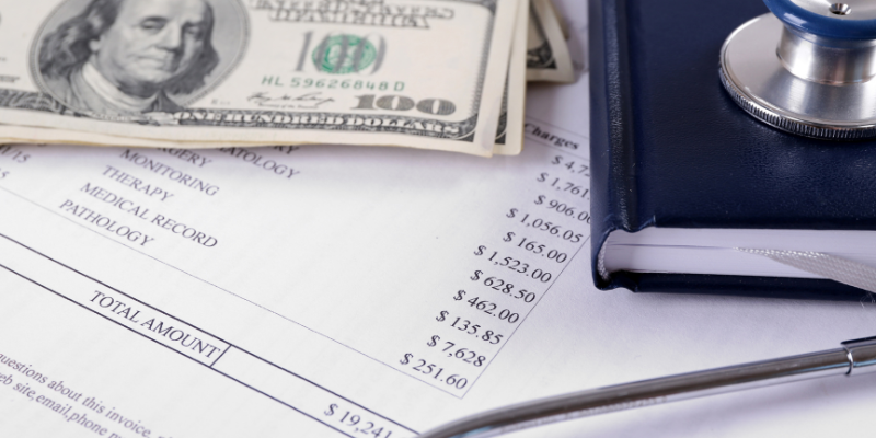 Up-close view of a medical bill with care cost breakdowns, $100 bills and a notebook.
