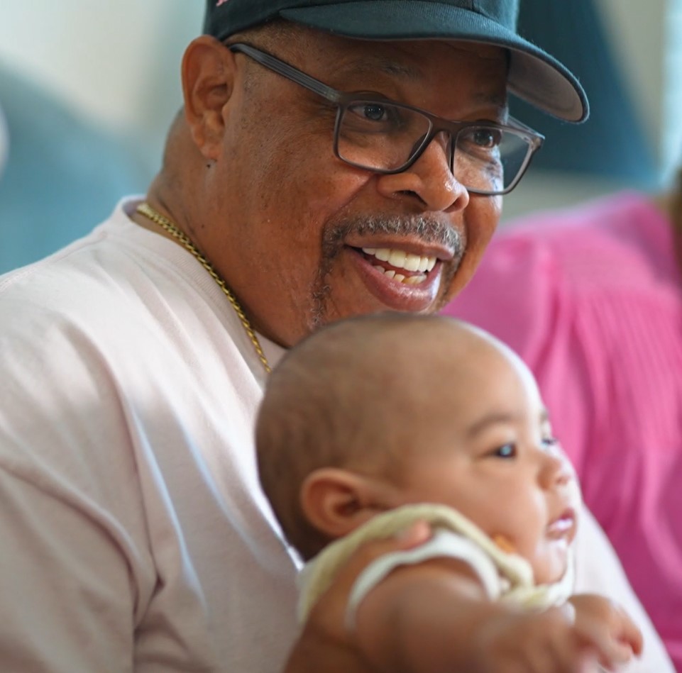 Vincent Delima smiles while holding a baby