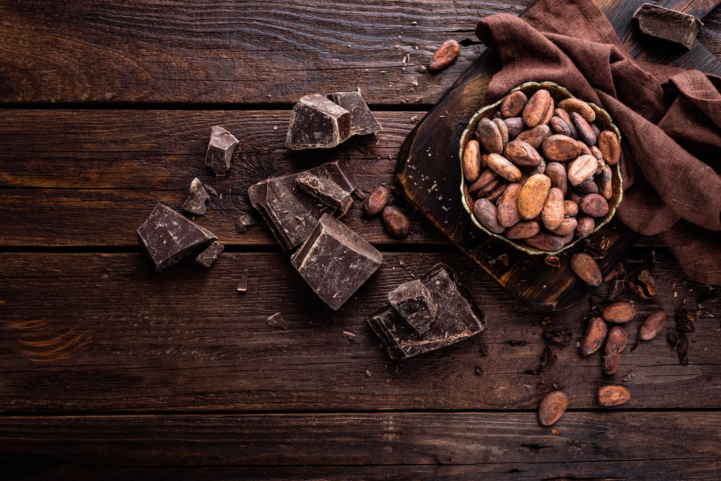 Pieces of dark chocolate and cacao beans on a dark wooden table.