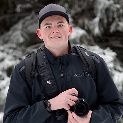 Konnor Sorg stands outside in the snow, smiling and holding a camera.