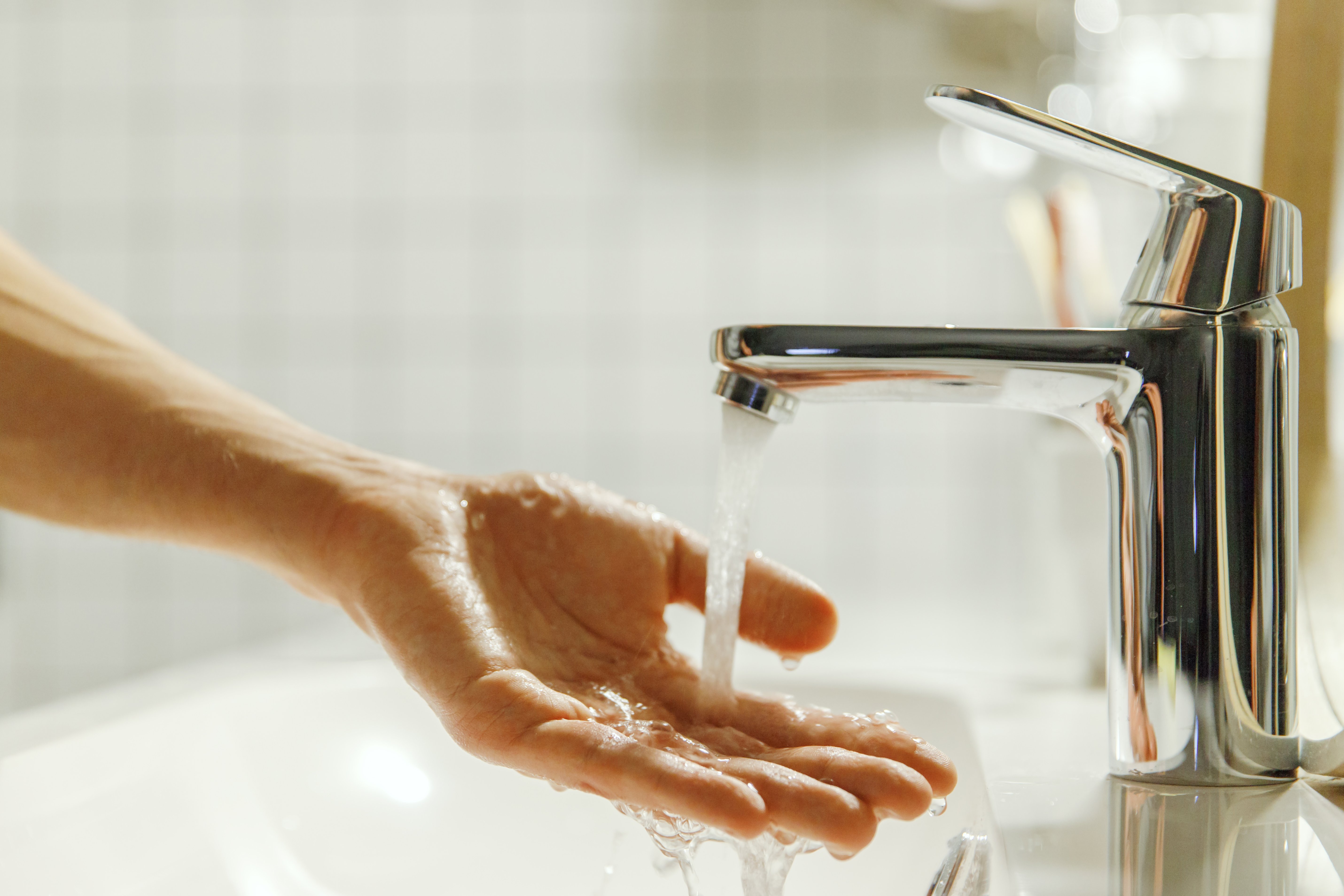 A person's hand being washed under a running bathroom faucet.