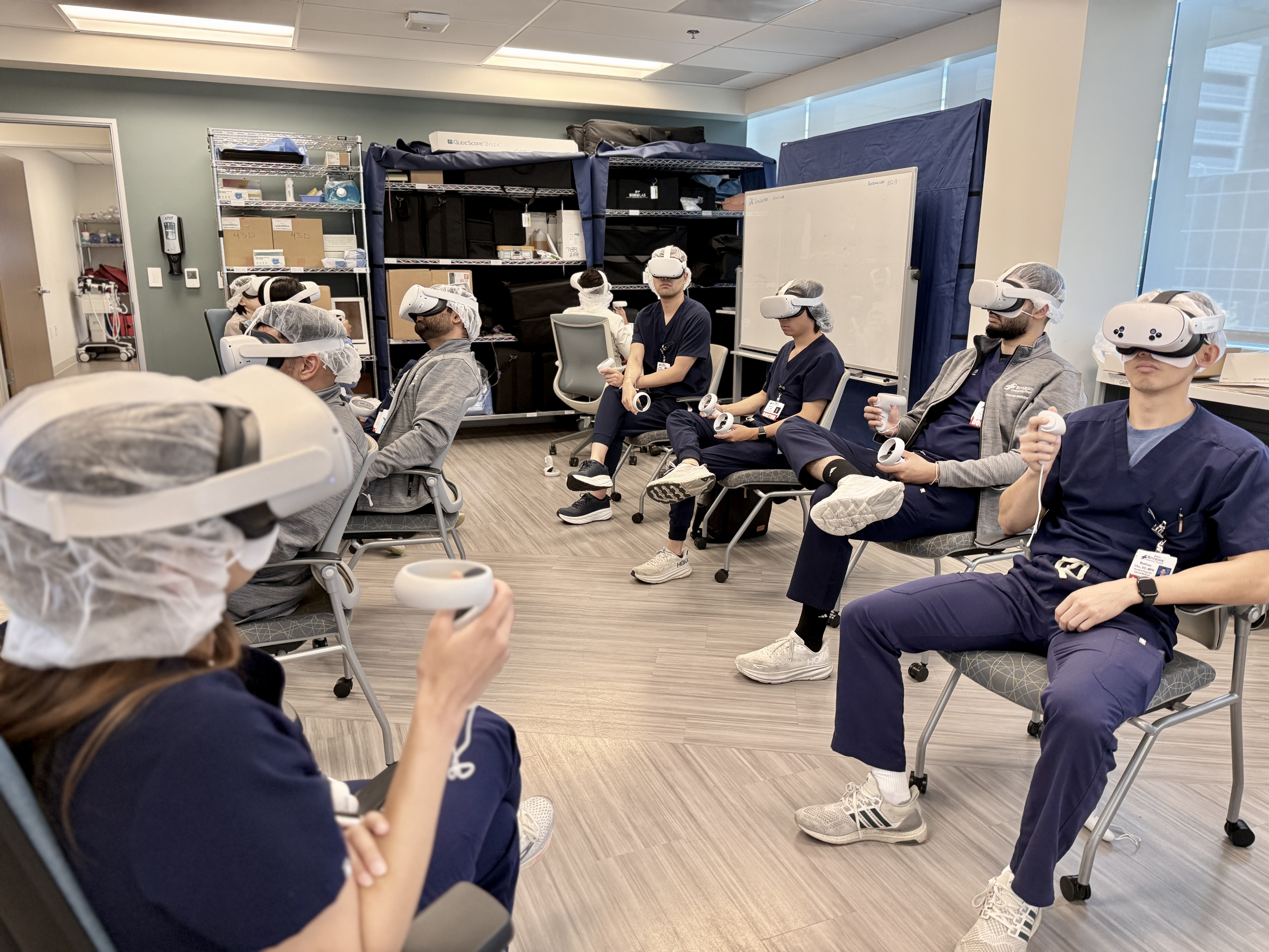 Graduate medical education physicians demonstrate the virtual reality system simulation by wearing goggles and holding a controller.