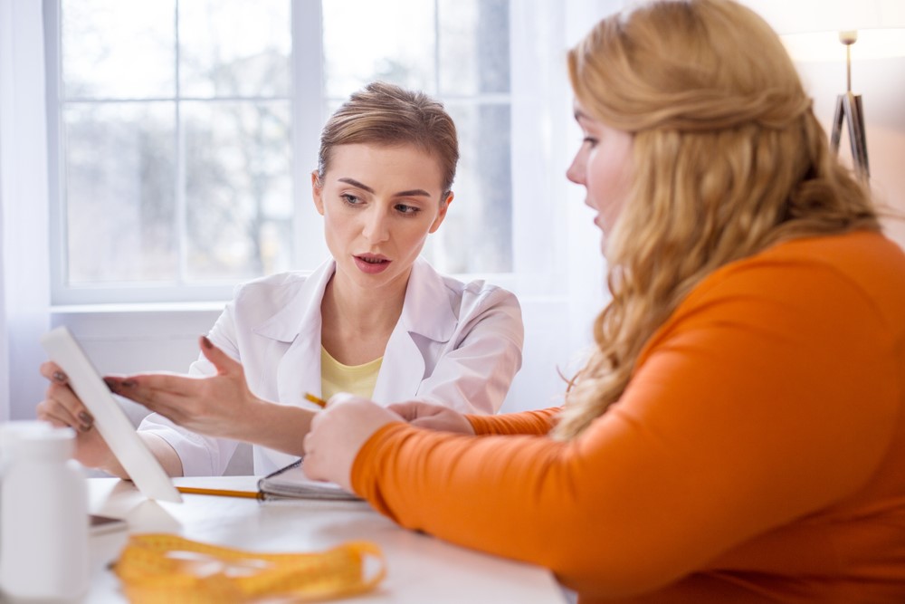 A doctor presenting information on a tablet to her female weight loss patient.