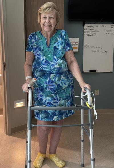 A woman standing in hospital gown with a walker and smiling