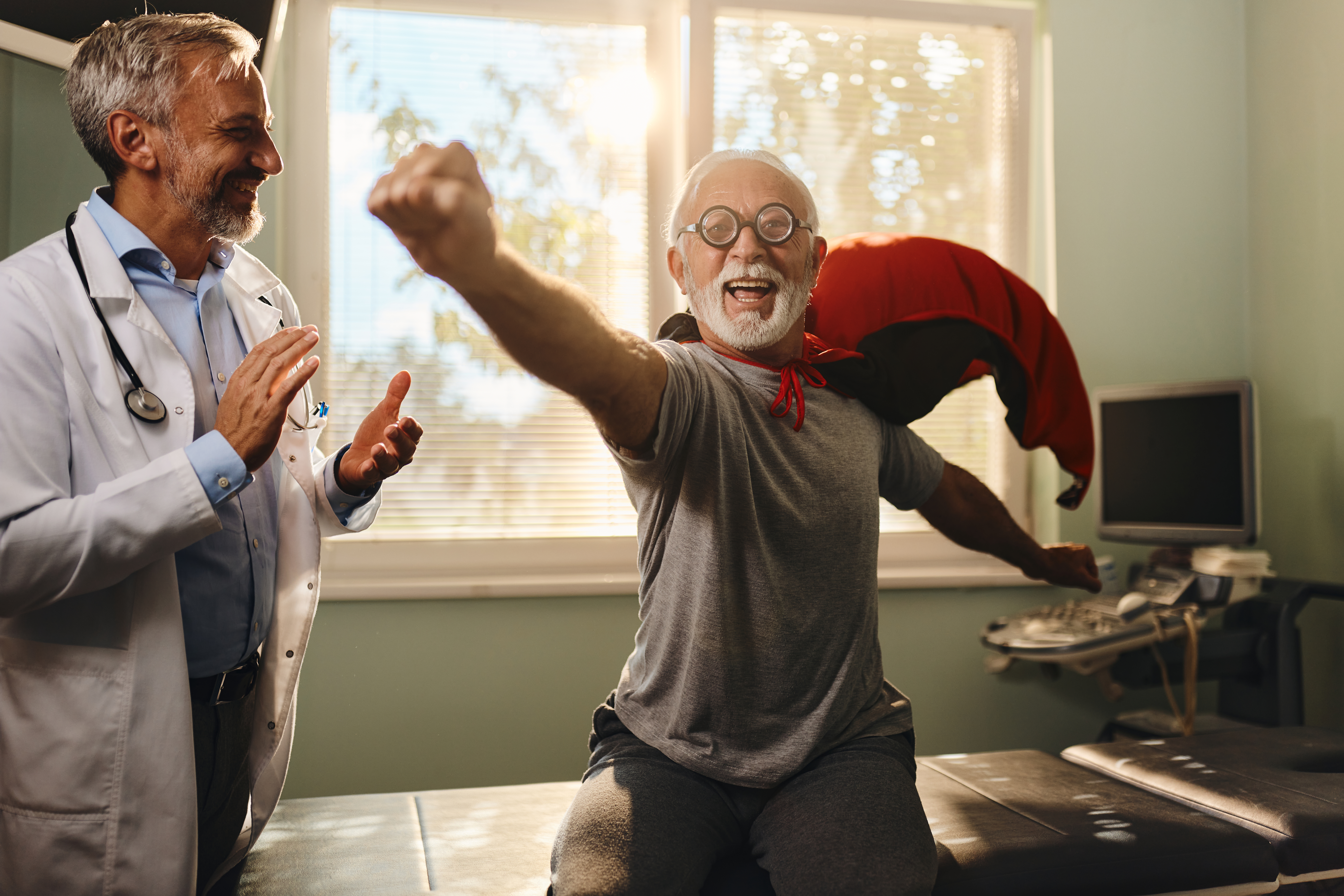 Elderly man in a cape talking to a doctor in a doctor's office.