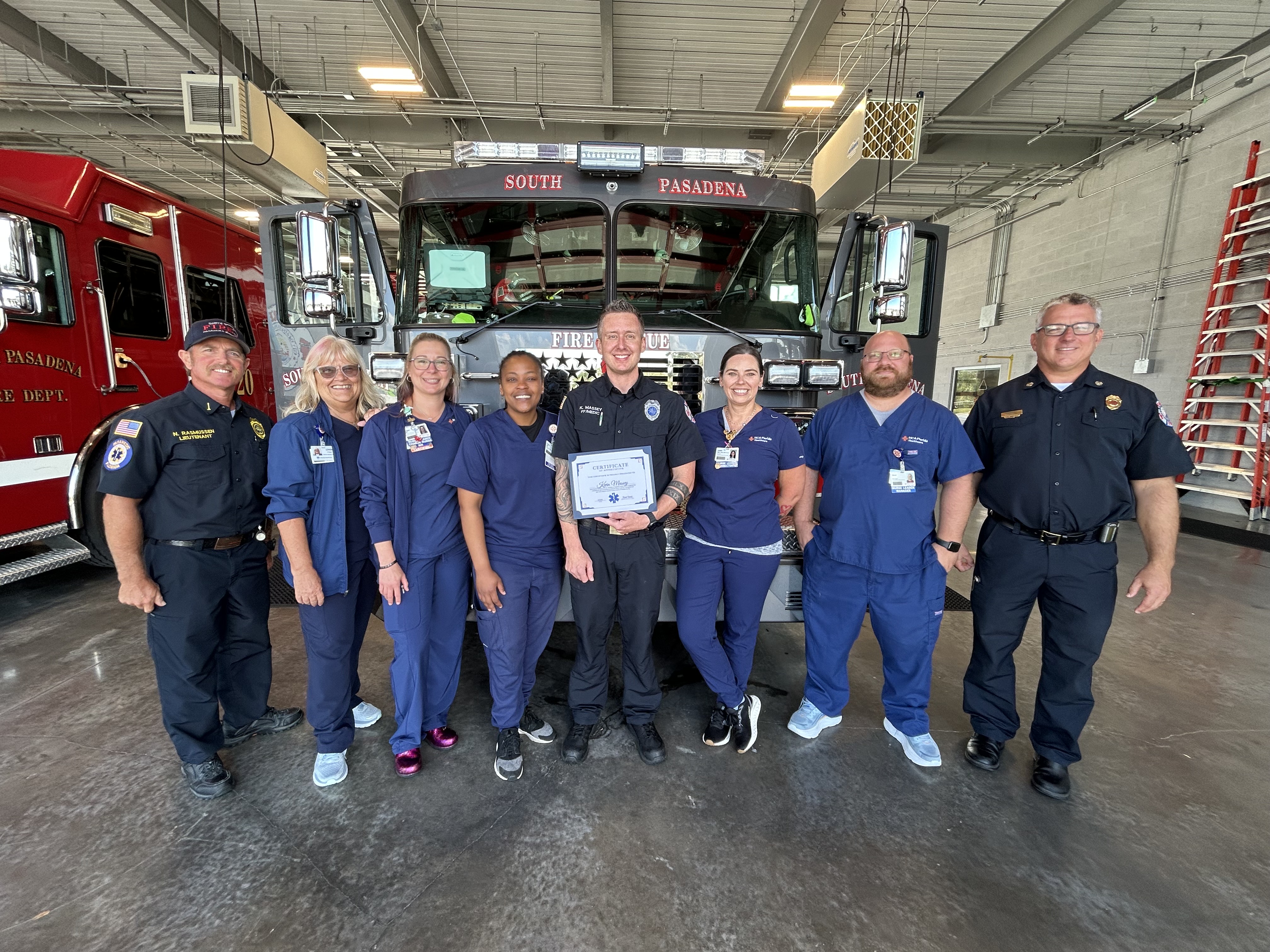 A group of paramedics standing in front of an emergency vehicle with an award/certificate.