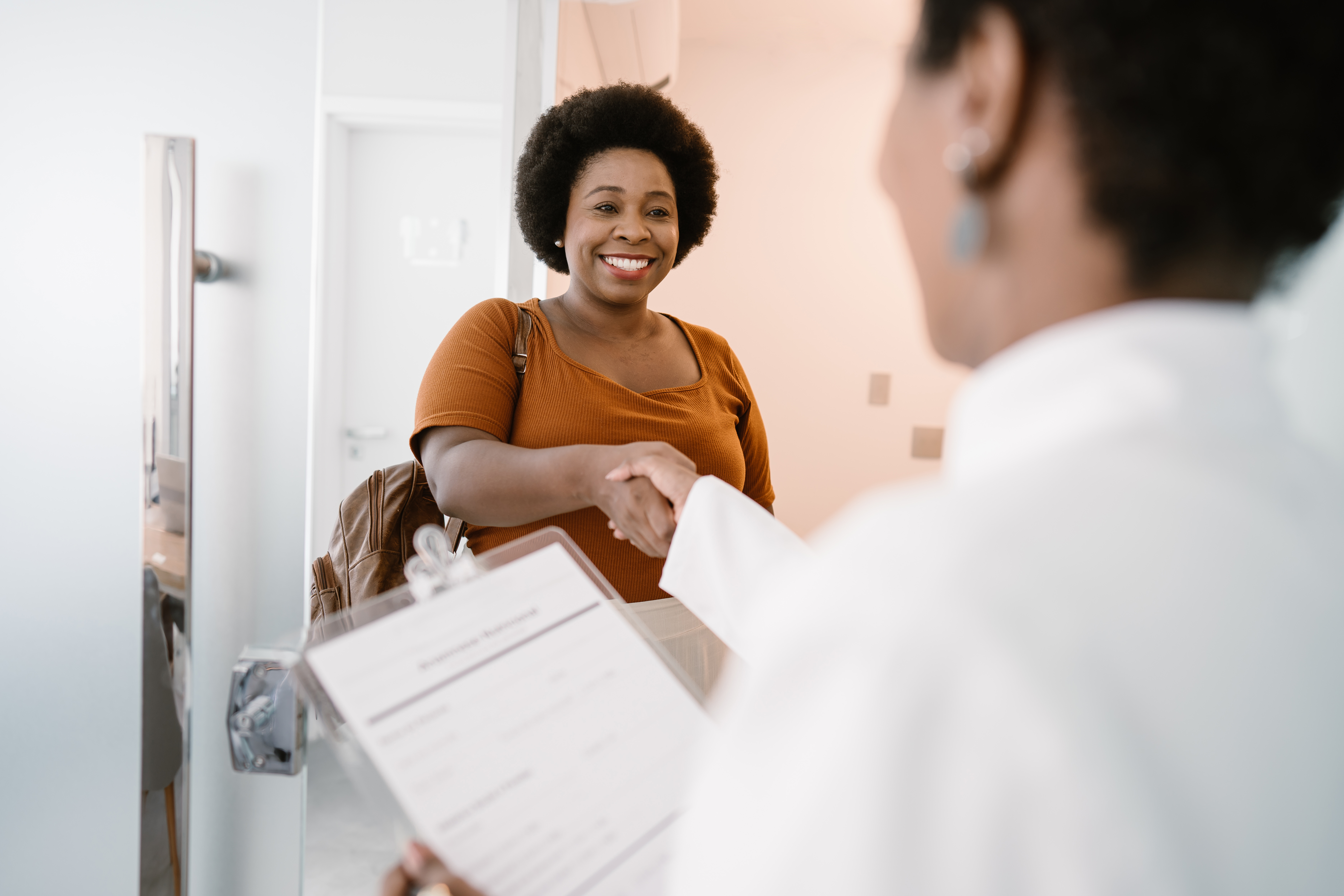 A woman arriving at the doctor's office and shaking hands with a medical professional.
