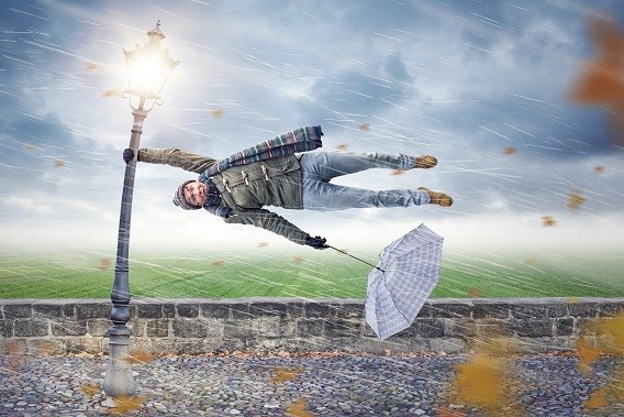 edited image of person with scarf hanging onto lamppost in heavy winds, being blown horizontally, with blown out umbrella in their other hand