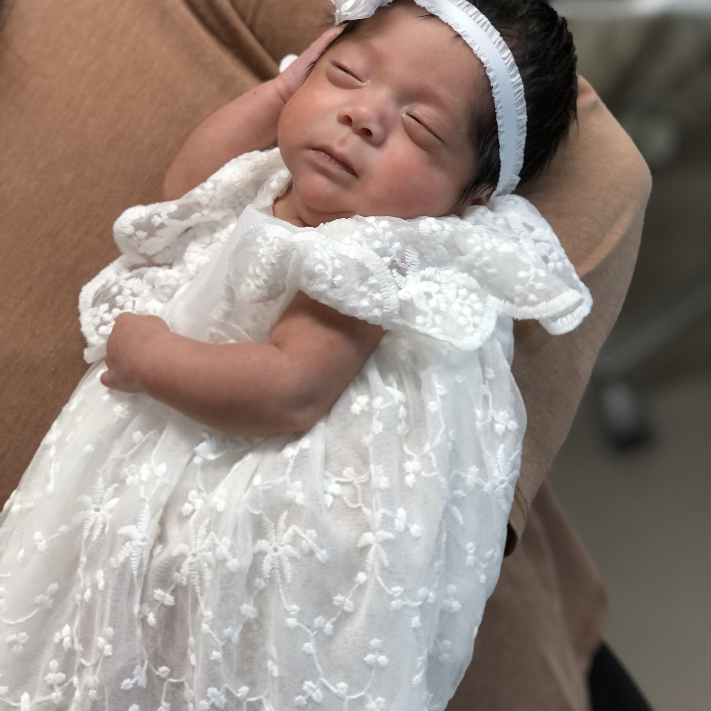 Baby Mia Ramirez in a white lace dress and headband.