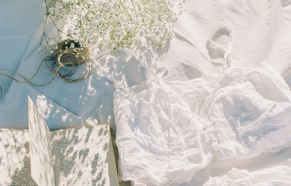 White bedsheets with a book, flowers, twine, and a knitted shirt.