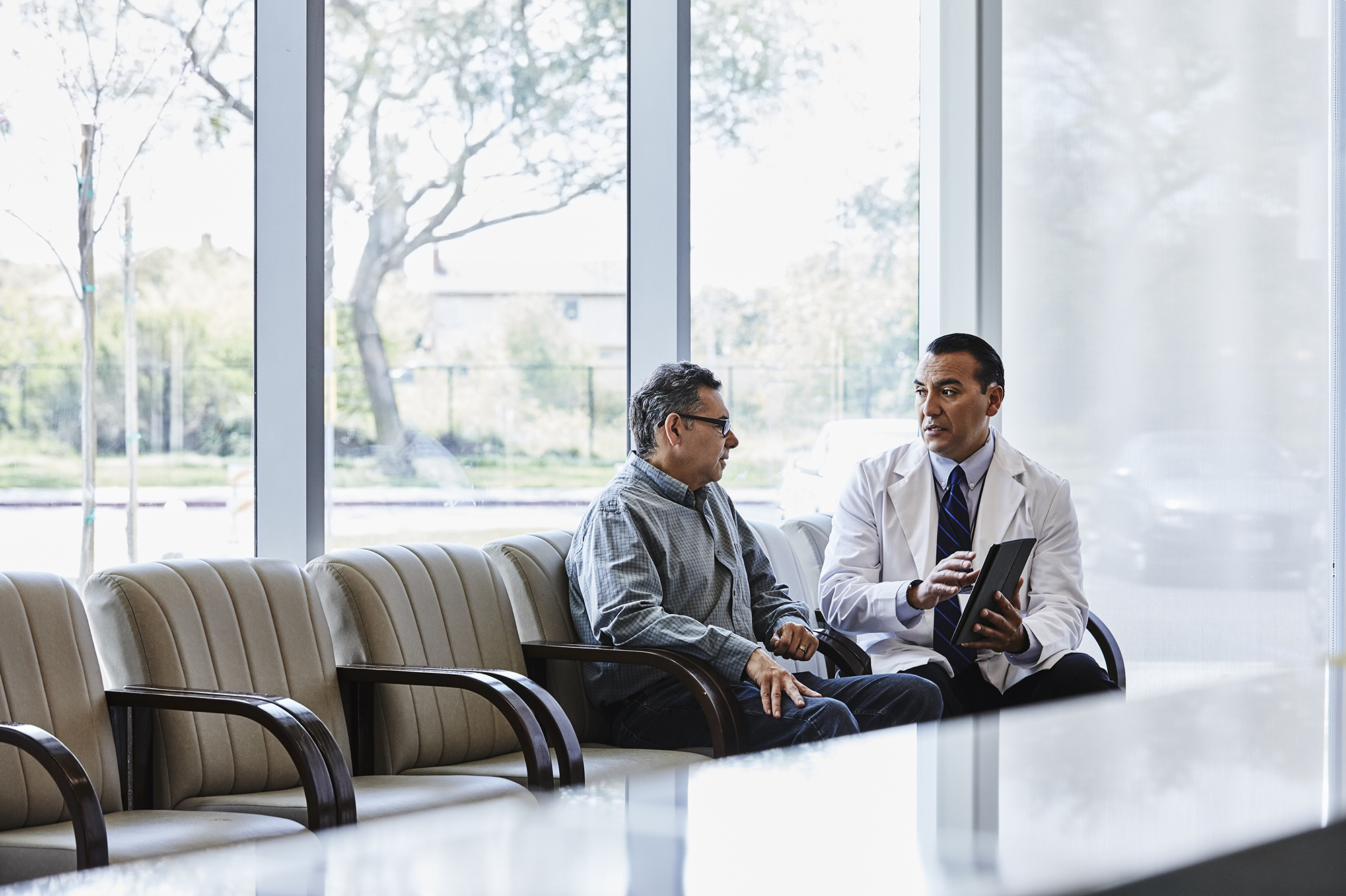 Doctor with digital tablet discussing with patient in waiting room.