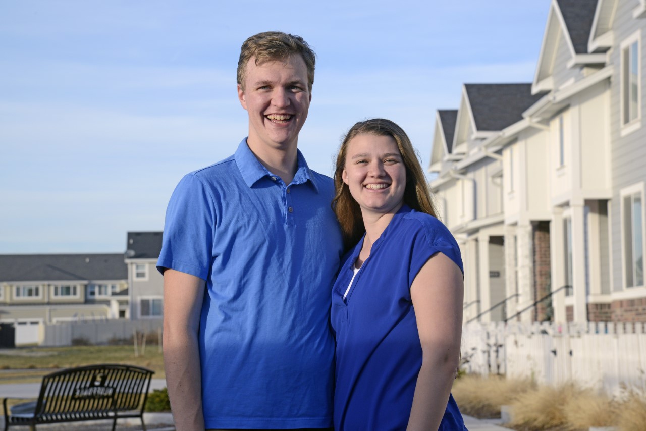 Noah and Korin Johnson pose in front of a row of townhouses.