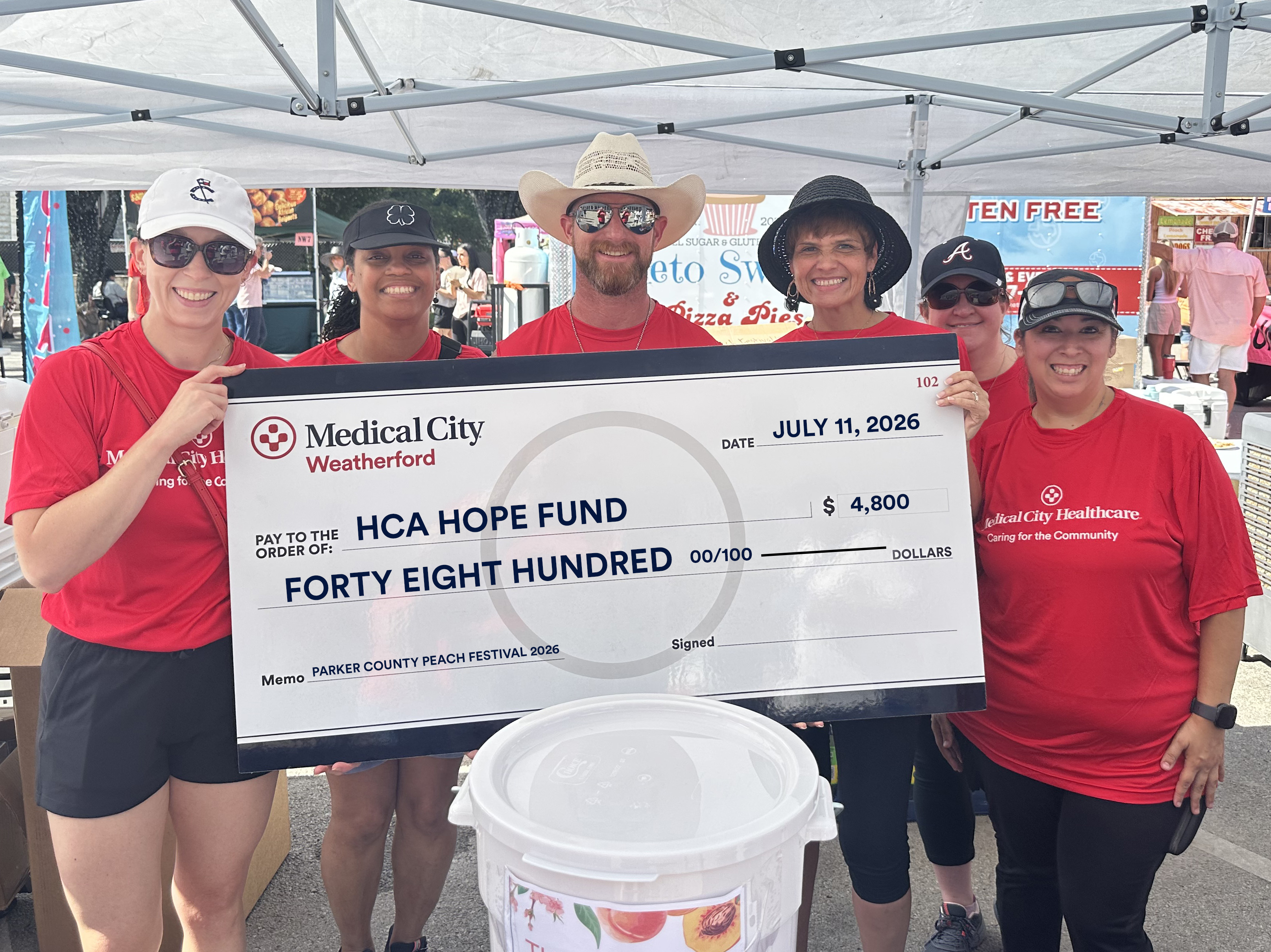 Medical City Weatherford employees smile while holding the check showing how much money they raised at the Peach Festival to donate to the Hope Fund.