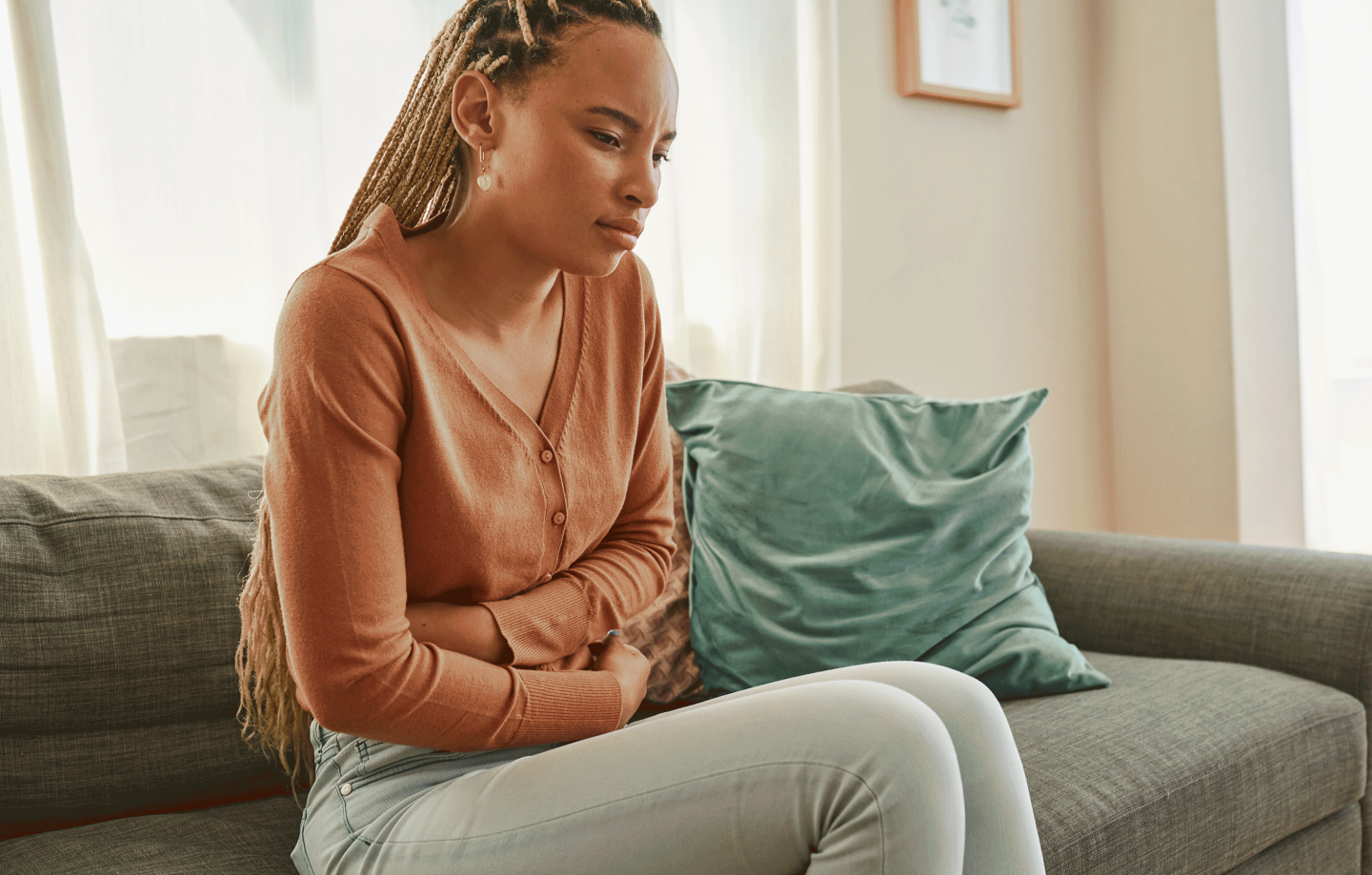 A woman seated on a couch clutches her abdomen in discomfort.