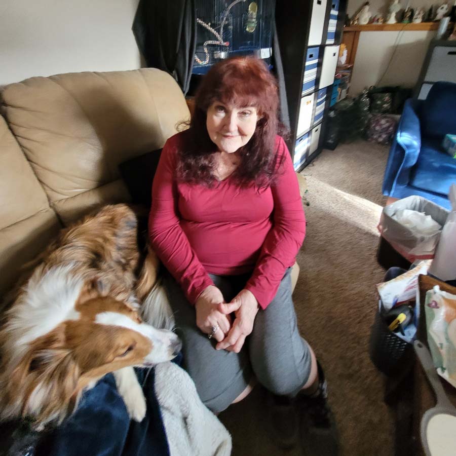 Trudy Murphy smiles while sitting on her couch with her dog.