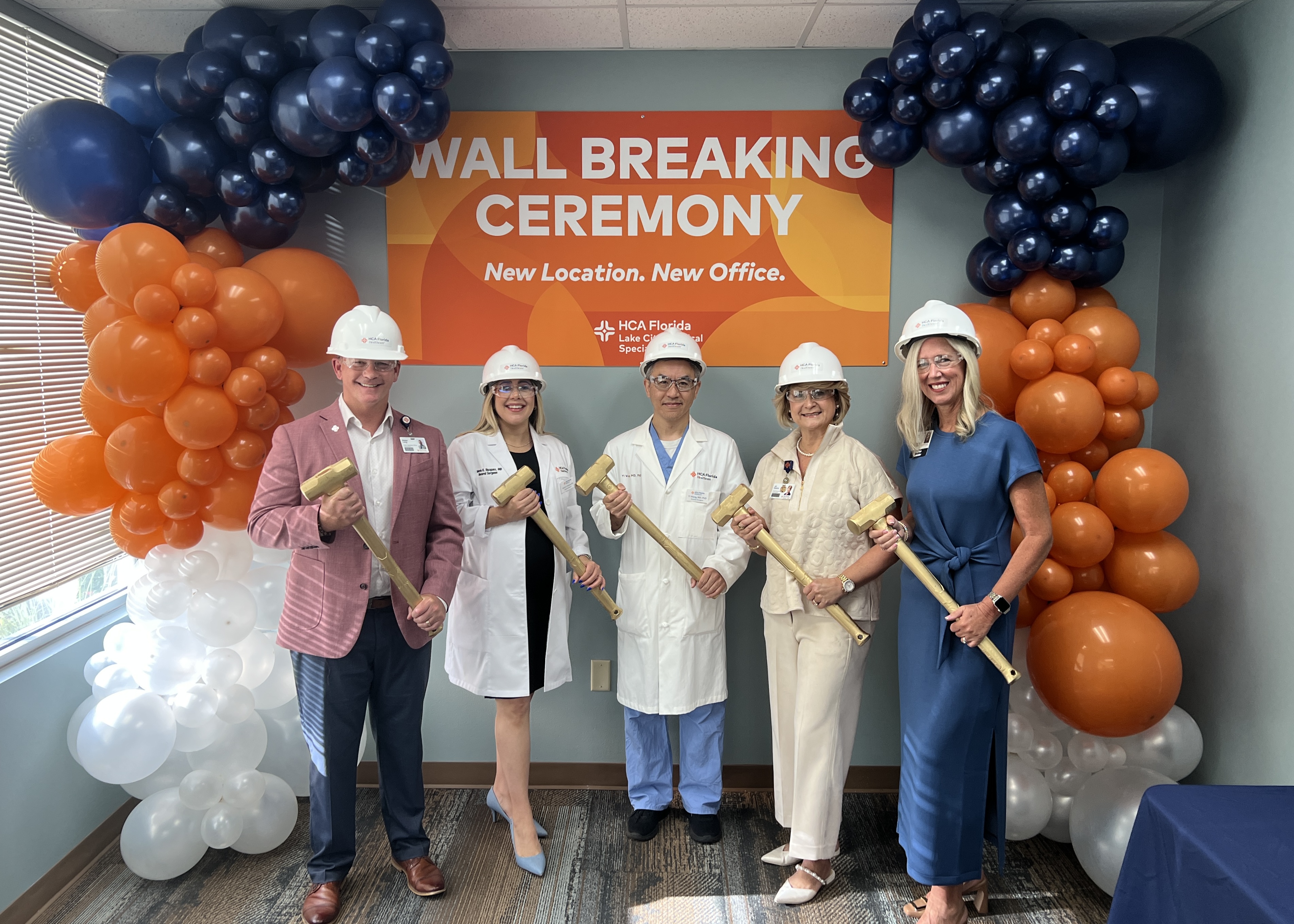 Lake City Surgical Specialists team members standing in office wearing hard hats and holding sledgehammers.