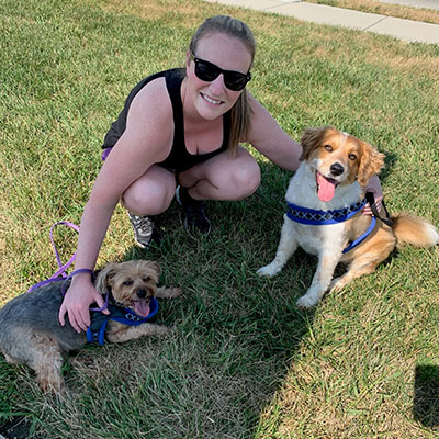 Geriann smiles while sitting in the grass with her two dogs.