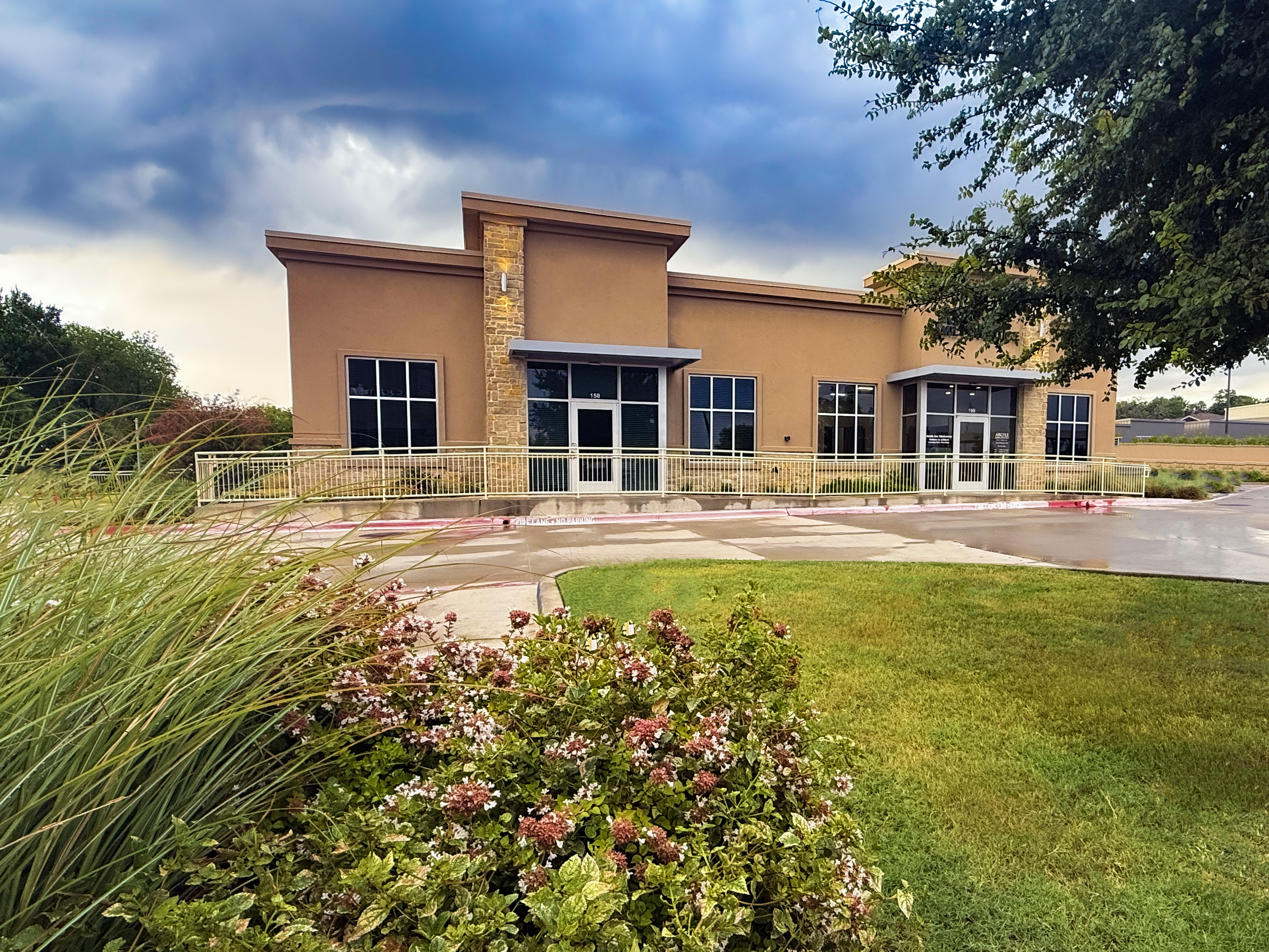 Exterior of Mental Health Therapy Argyle. A brown building with some grass and bushes across a curved drive.