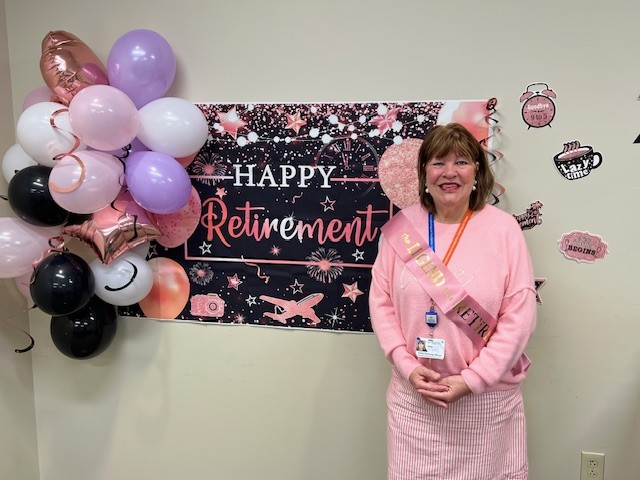 Amy Parator standing in front of a "happy retirement" banner and balloons