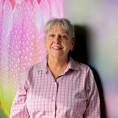 Janice standing in front of a painted wall wearing a pink checkered shirt.