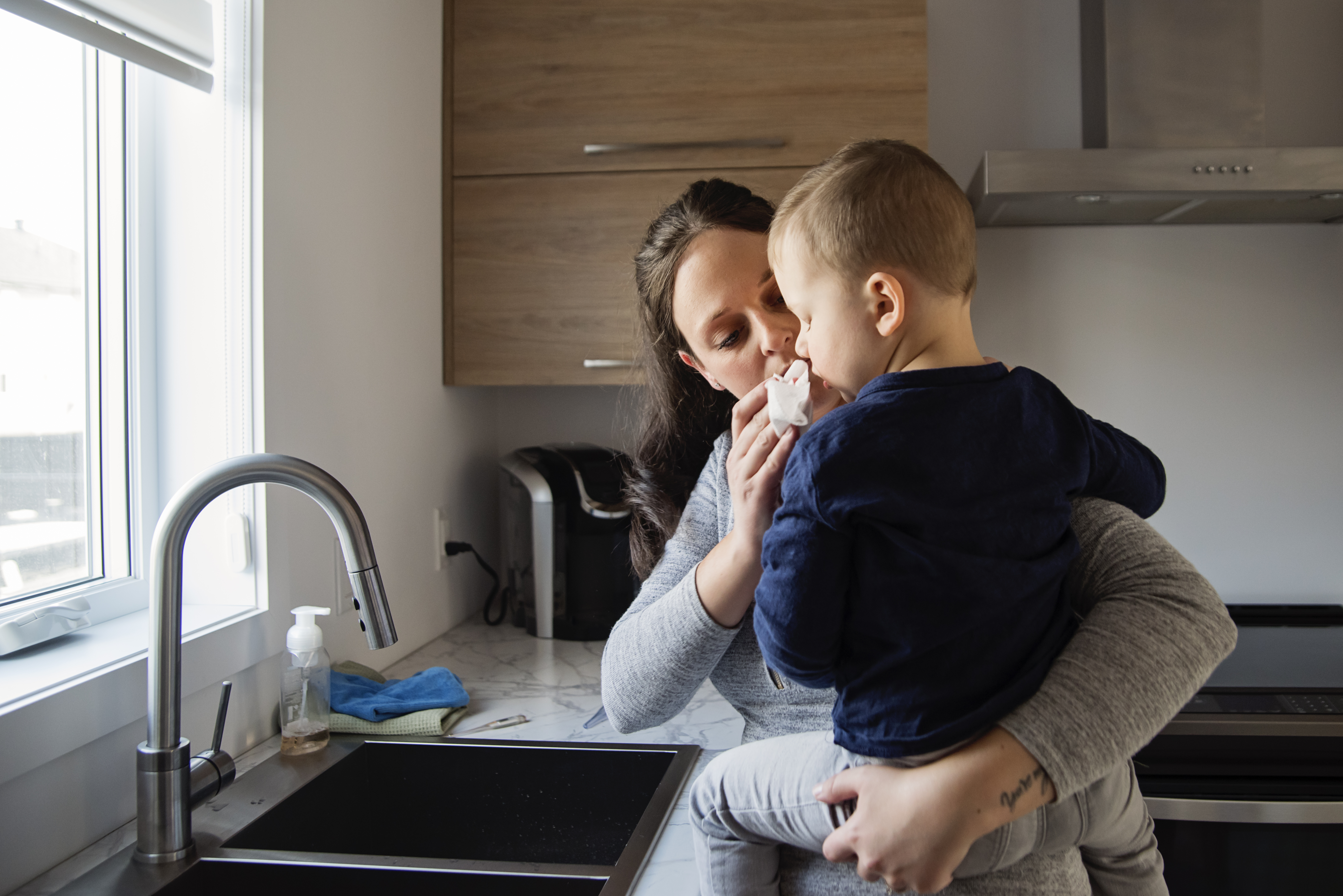 Woman at ktichen sink helps baby blow its nose.
