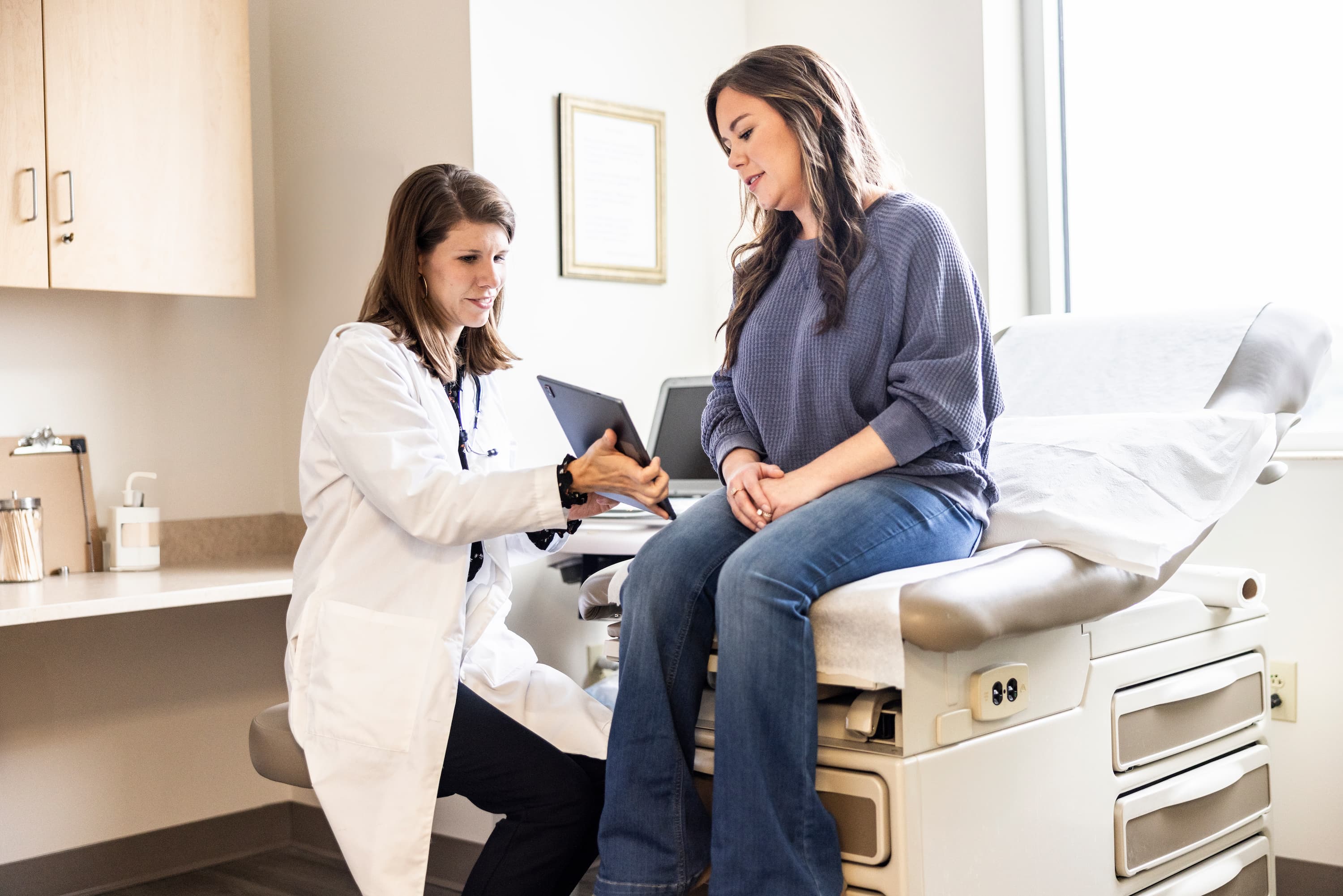 Healthcare provider showing test results on a tablet to a patient sitting on an exam table during a medical visit.