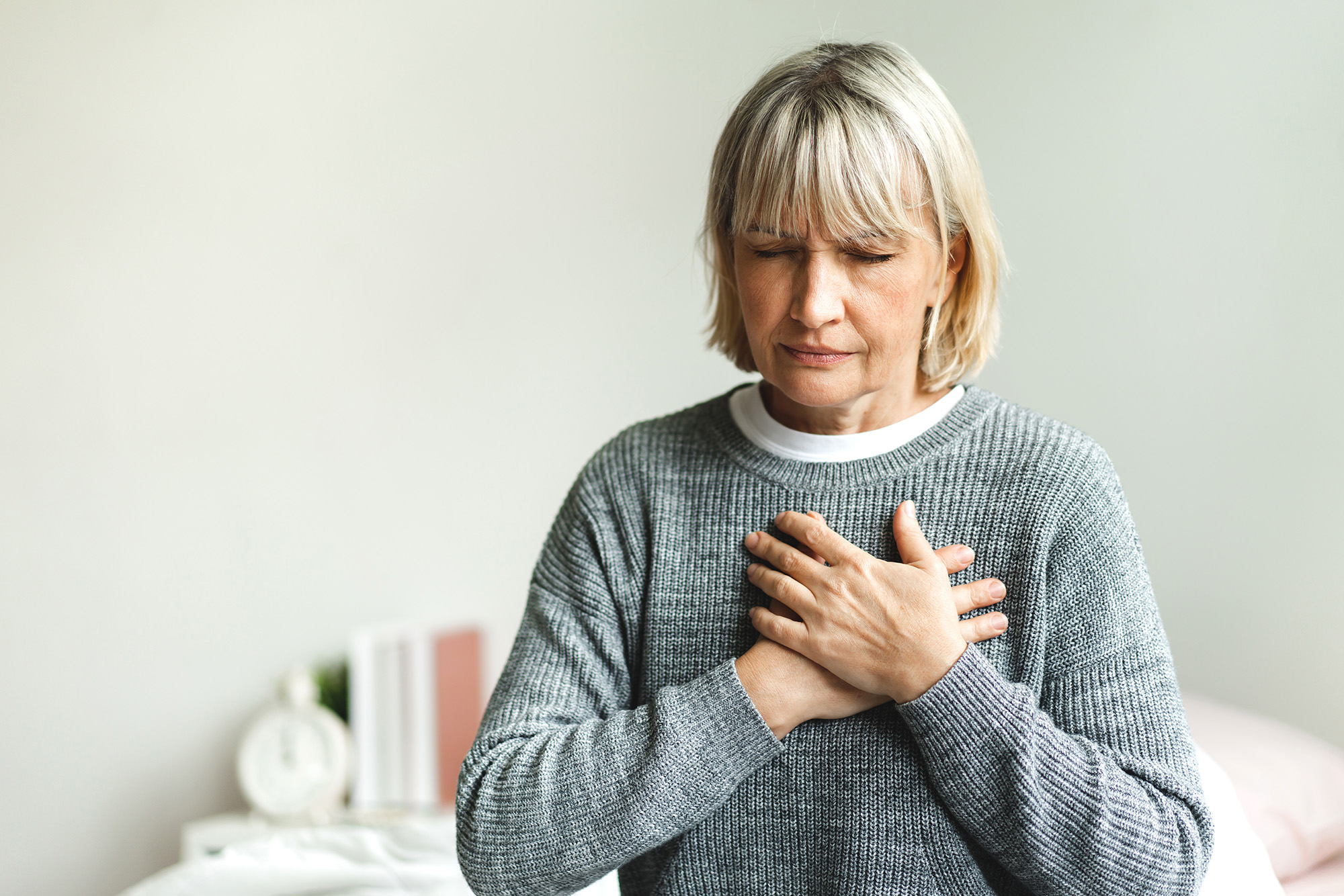 A seated woman holds her chest in discomfort