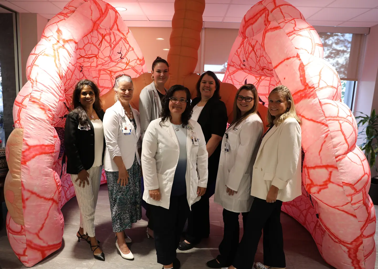 Picture shows seven women, most dressed in white coats, standing in front of a pink-and-red set of inflatable lungs.