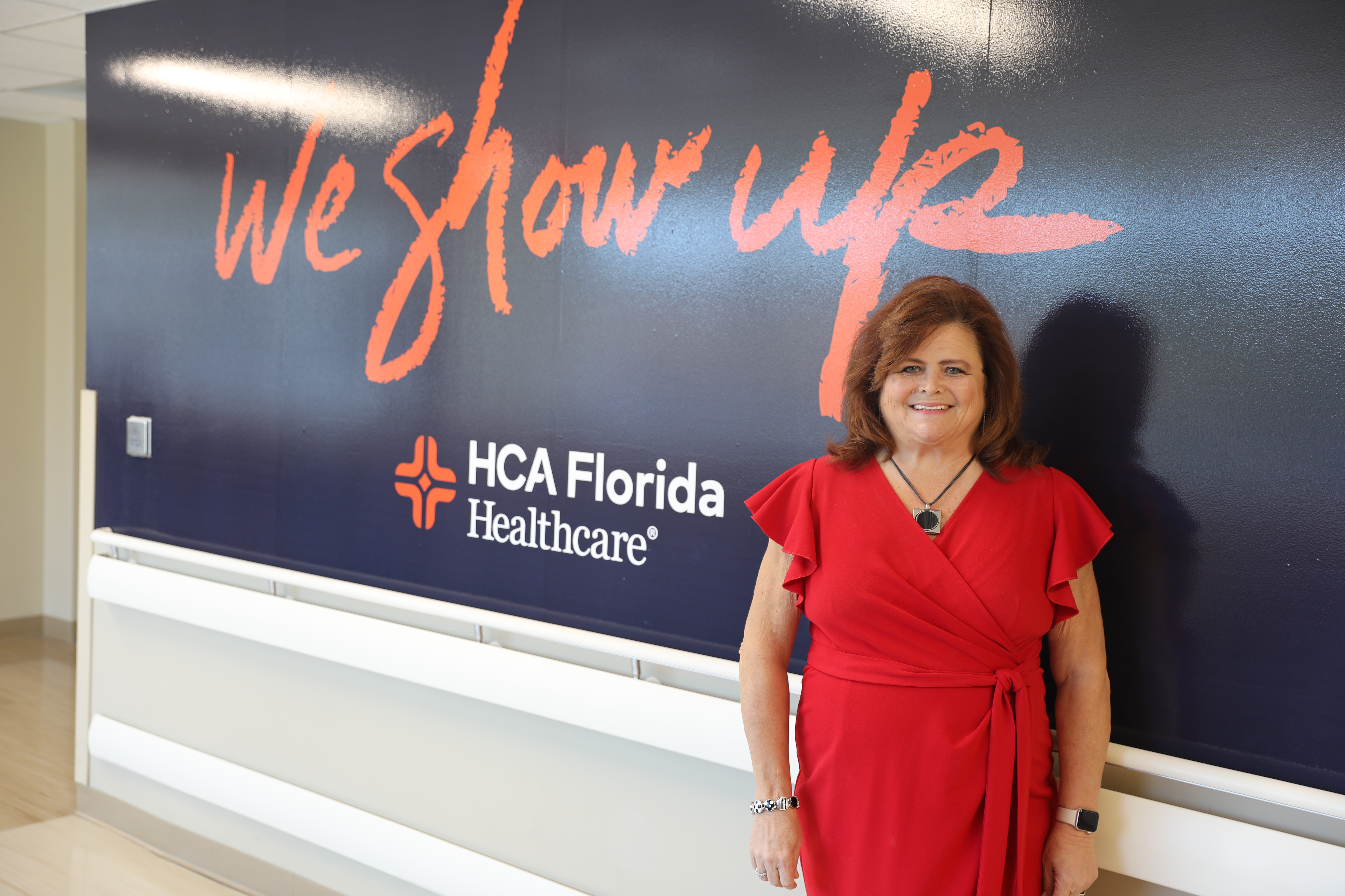 Michelle Hamilton standing next to We Show Up sign on wall in red dress