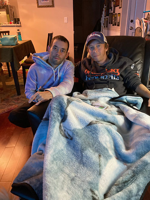 David and Matt Maddux smile while sitting together in David's living room.