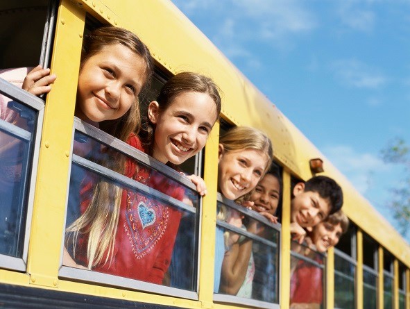 A group of children hanging their heads out of the windows in a school bus.