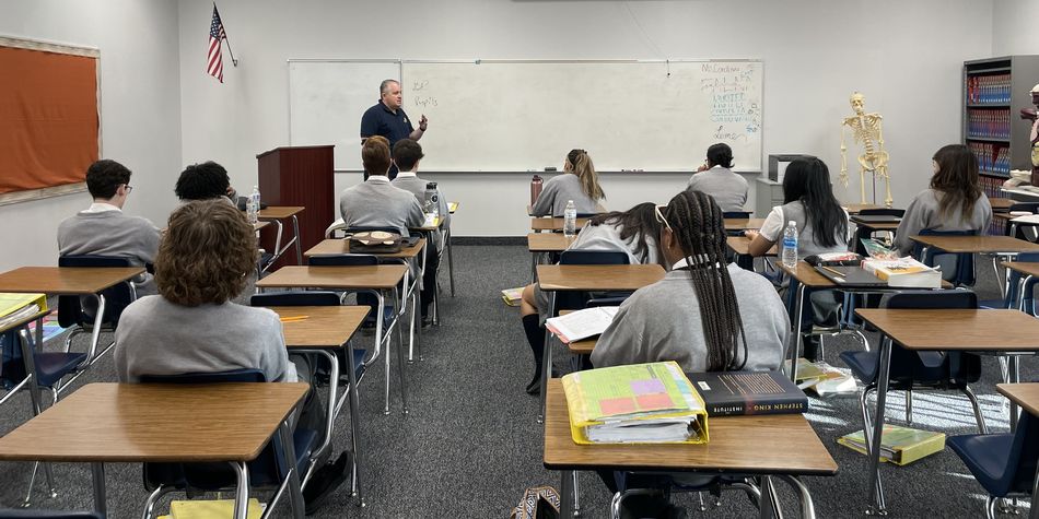 View from the back of a classroom of students with instructor, Mark Calabrese, at the front, near a whiteboard.